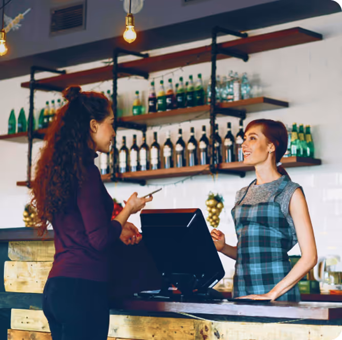 Two women standing at a bar talking to each other.