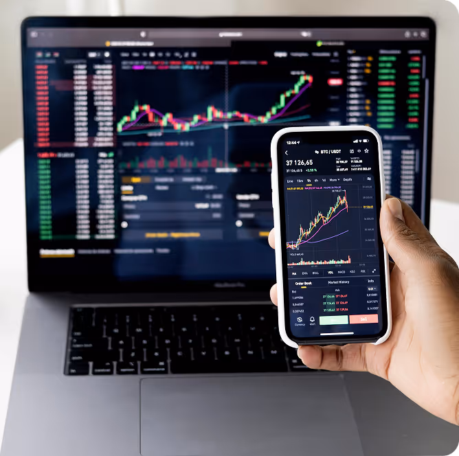 A person holding a cell phone in front of a laptop.