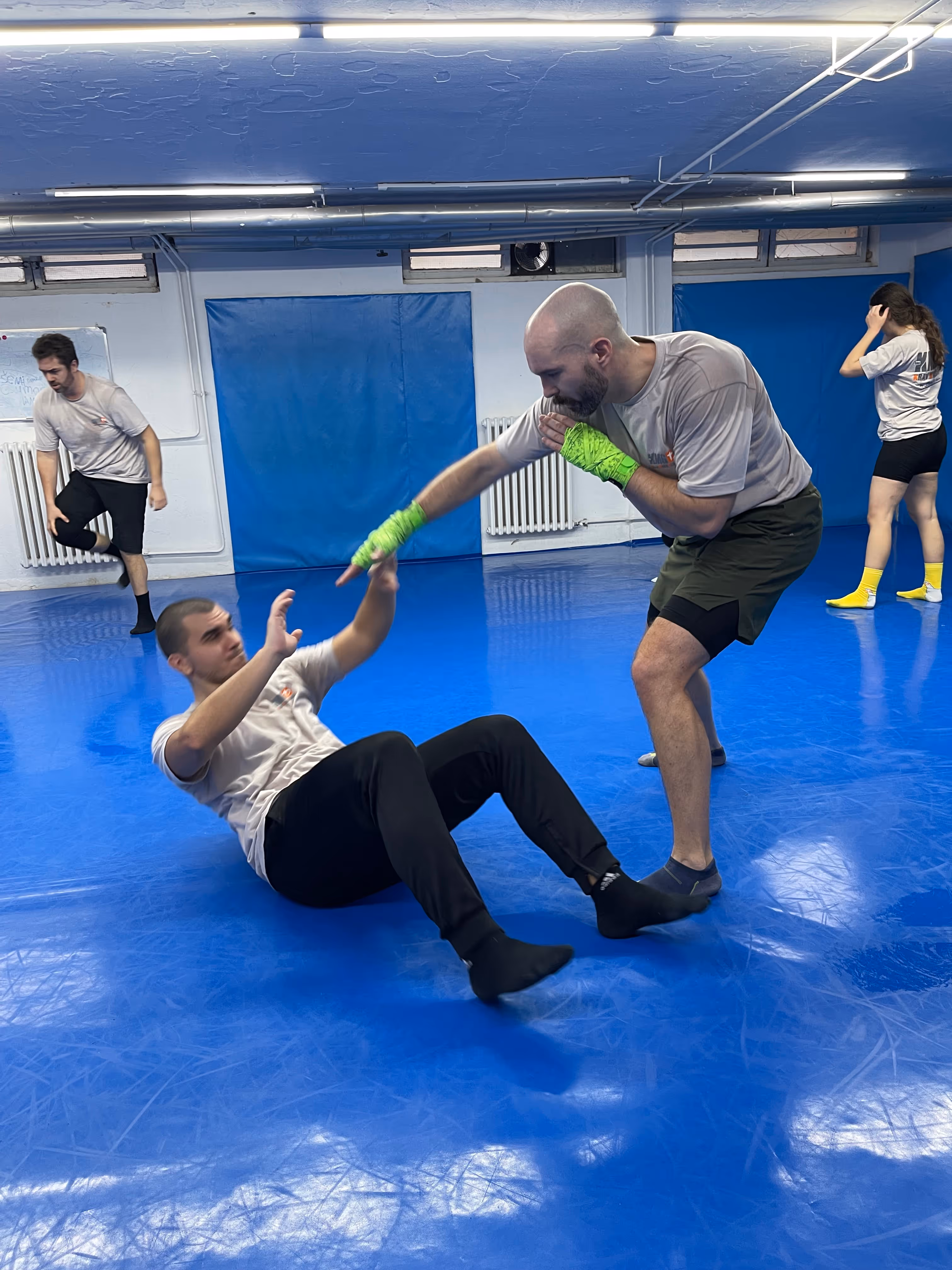 Polaznici Krav Maga treninga demonstriraju tehnike tokom testiranja za P nivo u sali, pod nadzorom instruktora