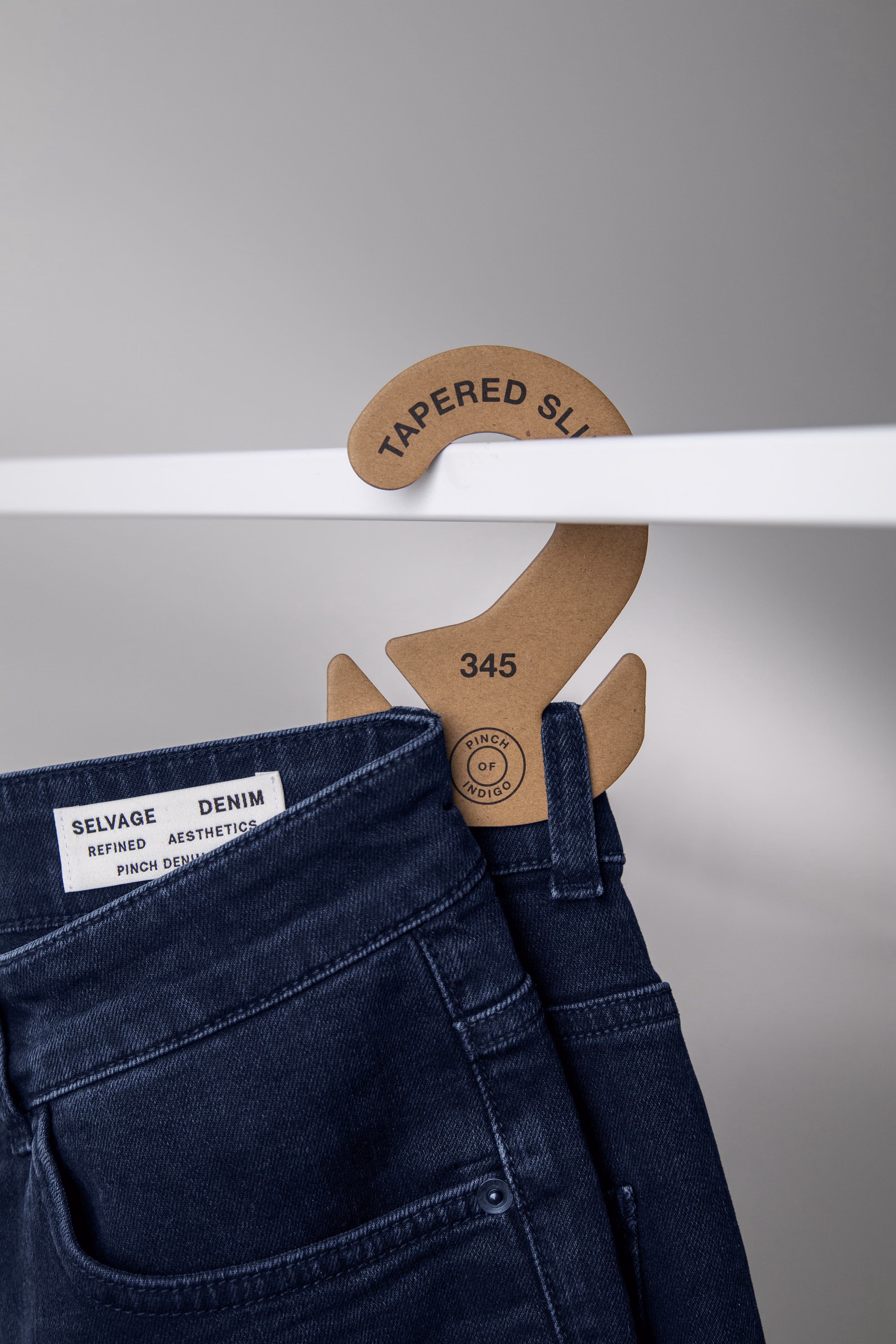 Dark blue denim pants on a paperboard hanger labeled "Tapered Slim," with a minimalistic design and a clean, modern aesthetic.