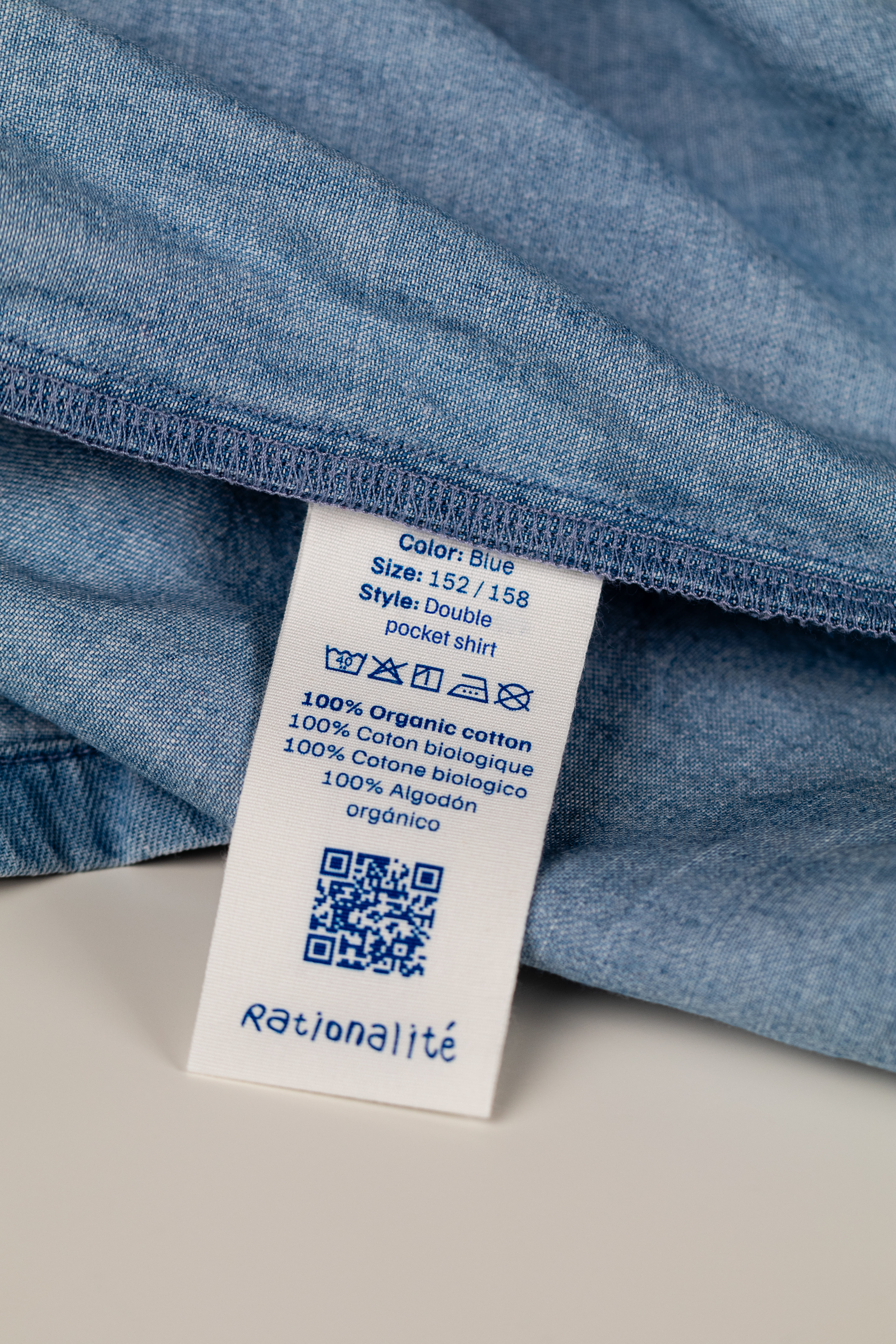 Close-up of a denim shirt displaying a woven care instruction label for apparel identification and compliance.