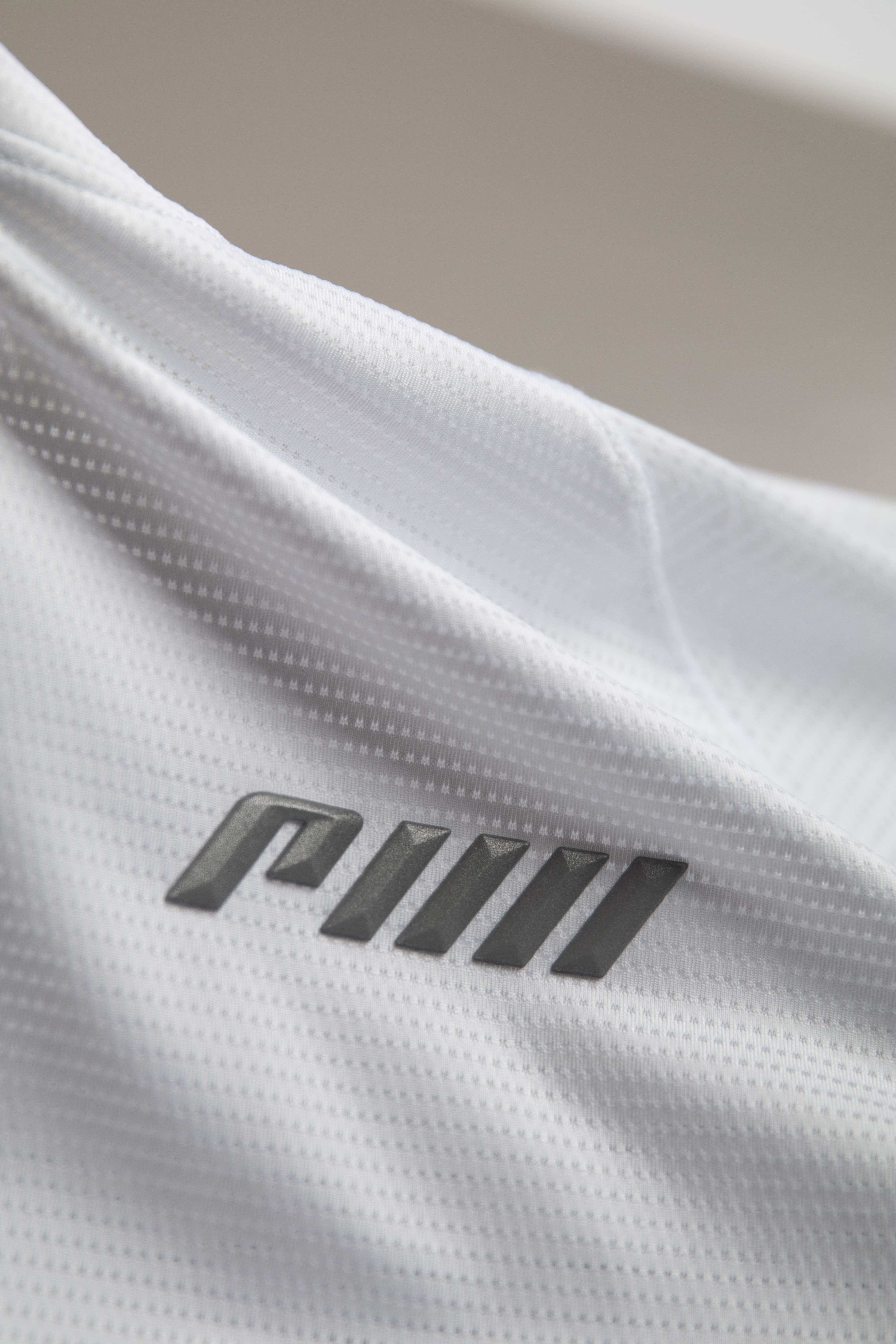 White activewear shirt featuring a prominent raised 3D logo on the front, highlighting tactile, dimensional trim that brings a soft, playful aesthetic to a contemporary performance garment.