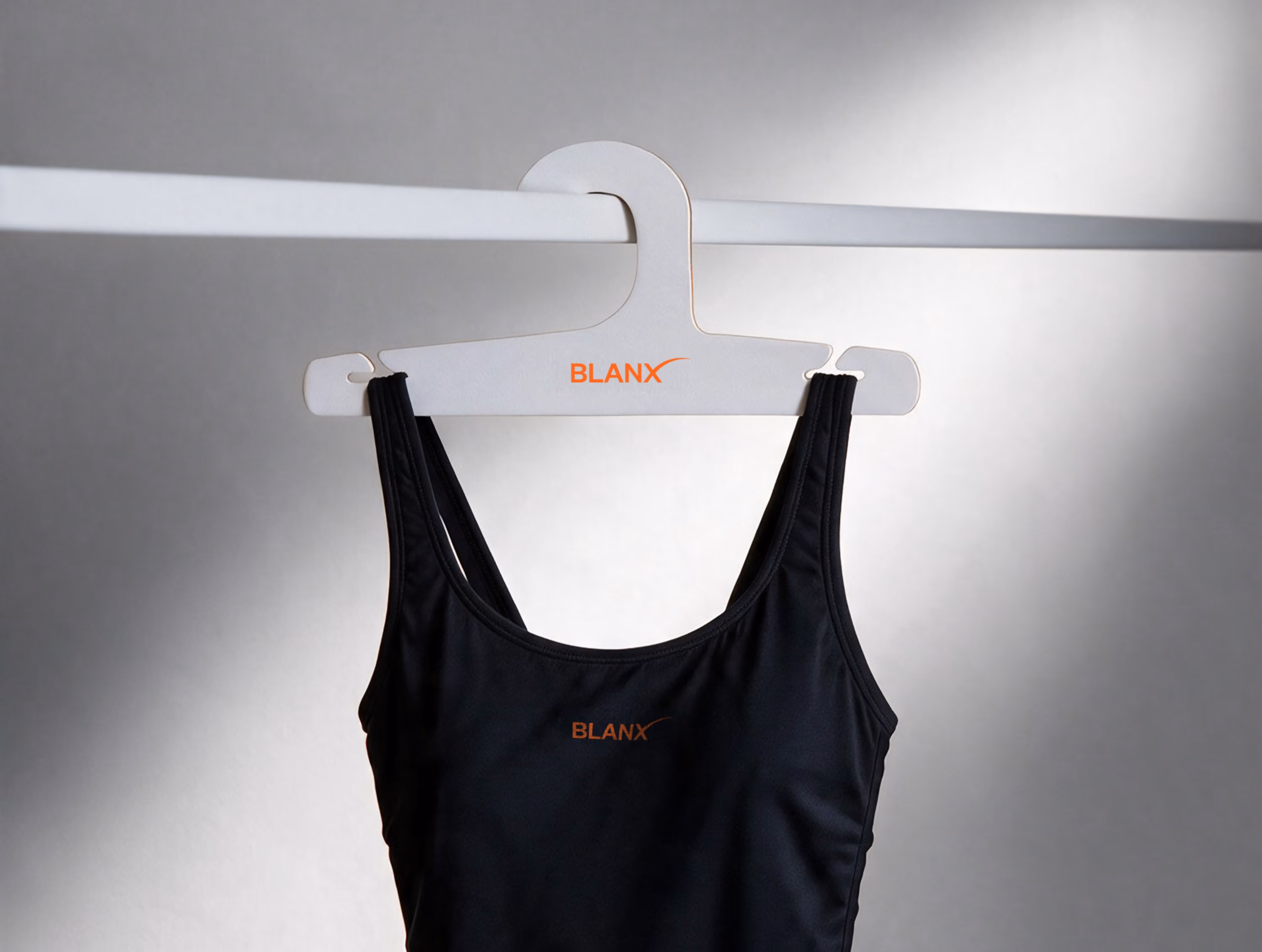 Black swimsuit hanging from a white BLANX hanger on a clothing rail against a gray wall, showcasing minimalist swimwear presentation and branded hanger design.