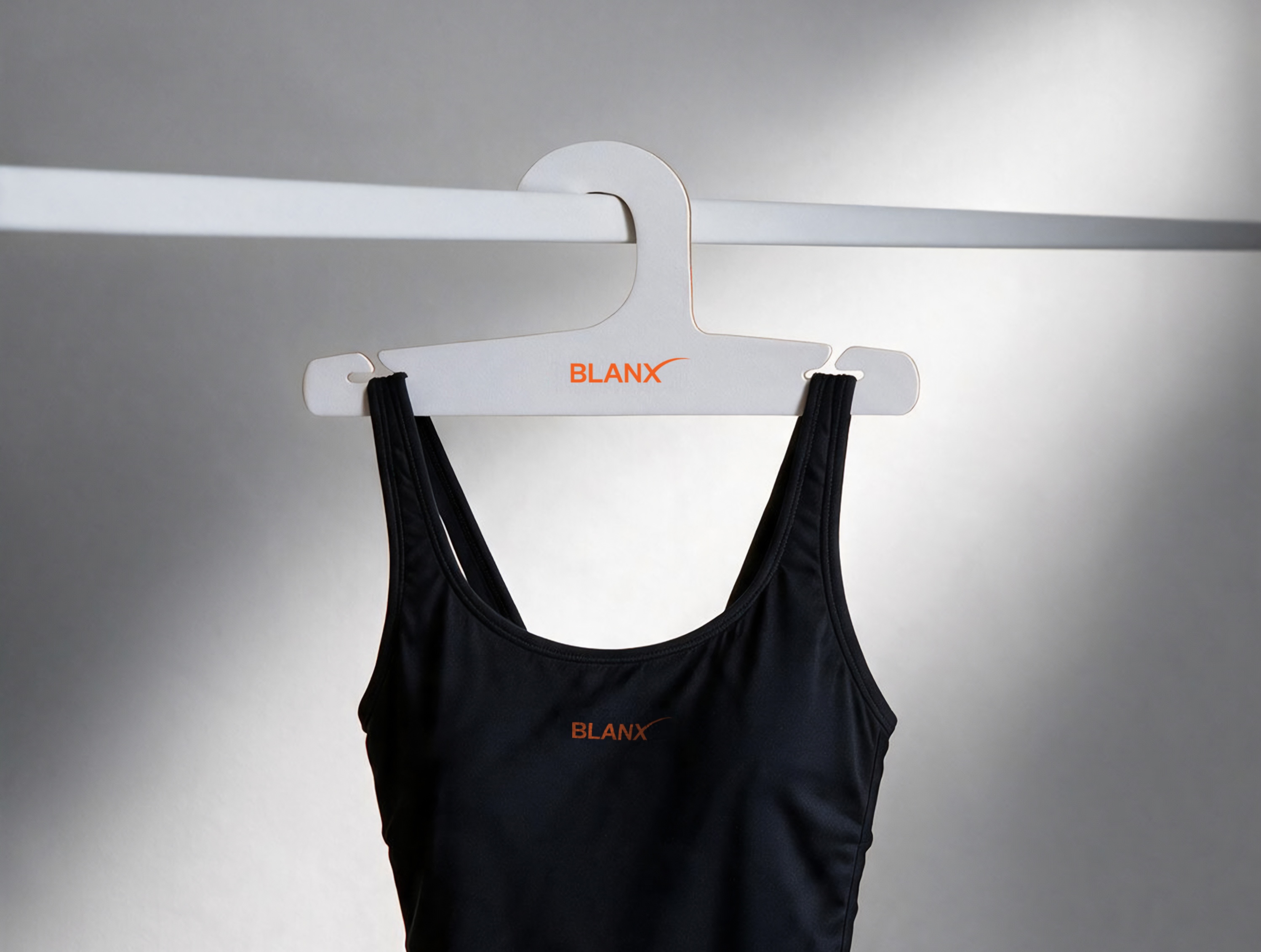 Black swimsuit hanging from a white BLANX hanger on a clothing rail against a gray wall, showcasing minimalist swimwear presentation and branded hanger design.