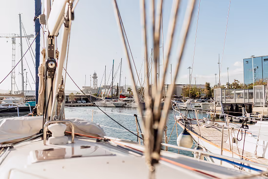 View from the deck of a sailboat docked at a marina with other boats and a lighthouse in the background under a clear sky.