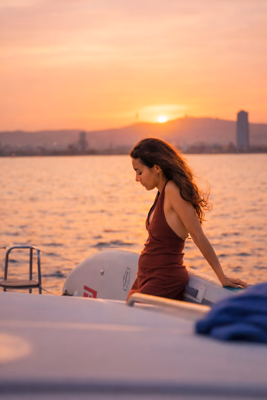 Smiling couple embracing on a boat at sunset with city skyline in the background.
