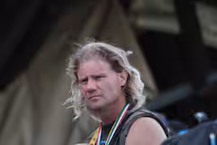 Man with long blonde hair wearing a black sleeveless shirt and a medal around his neck.