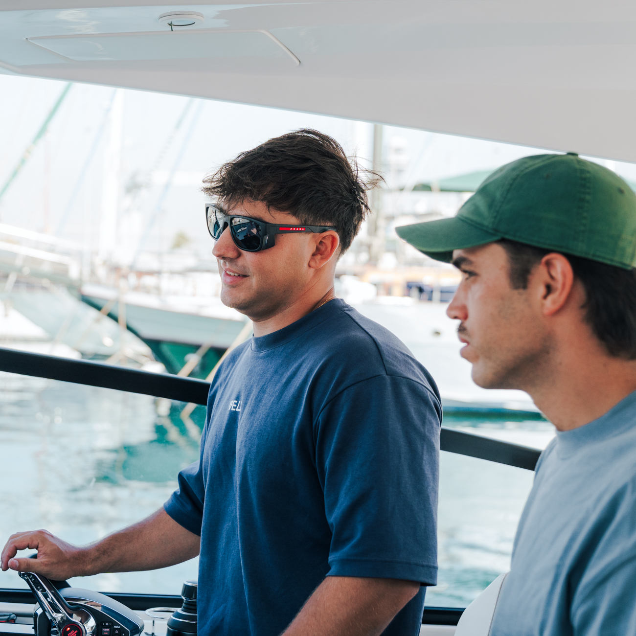 Three smiling people enjoying a sunny day sailing on calm water with a city skyline in the background.