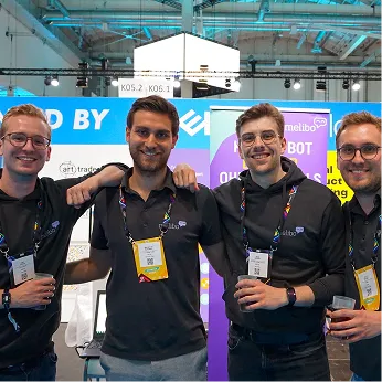 Four smiling men wearing black shirts and name badges standing together at an event booth.