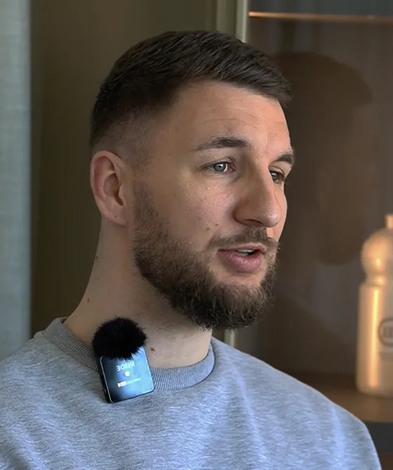 Bearded man speaking with a lapel microphone clipped to his gray shirt.