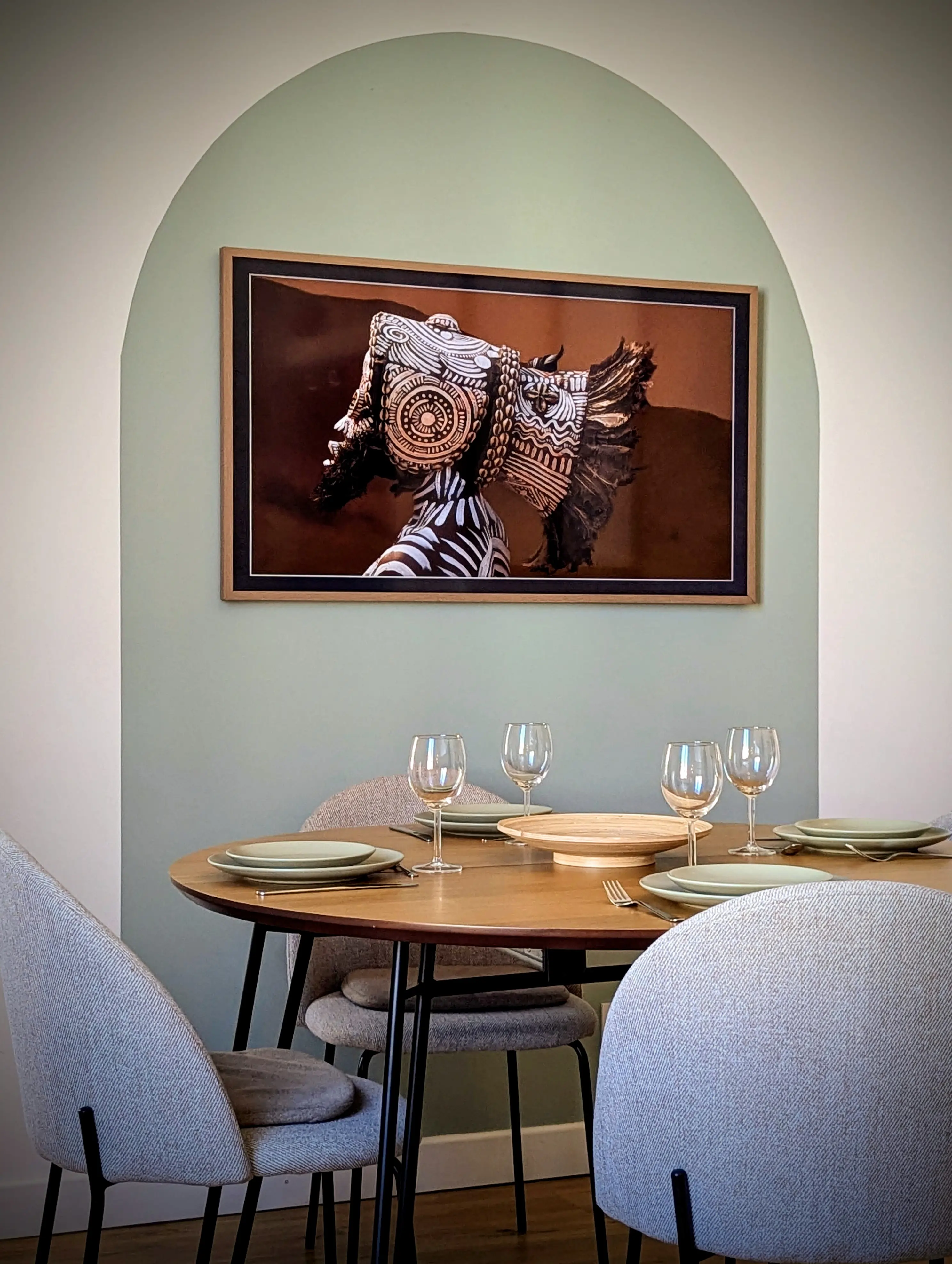Décoration murale avec arche peinte en vert sauge et grand cadre photo art ethnique au-dessus d'une table à manger.