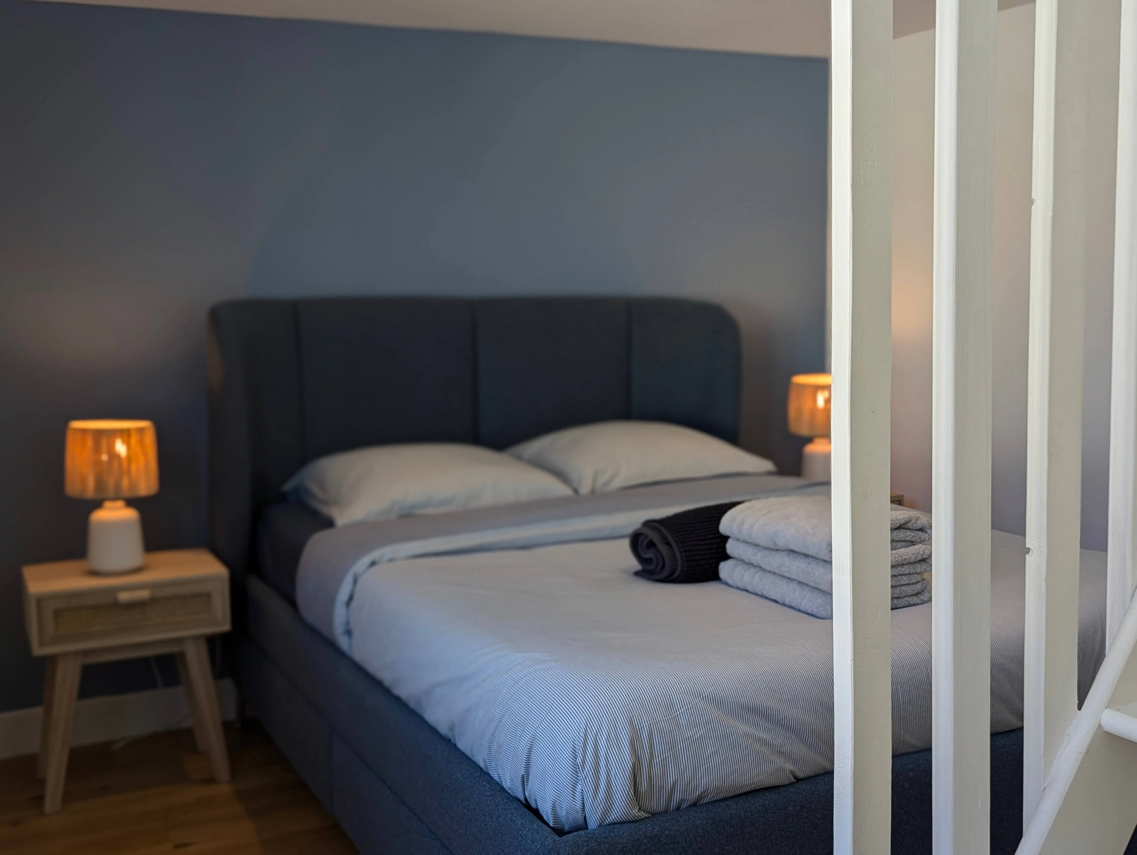Chambre parentale cocooning vue derrière un claustra blanc, lit tête de lit bleu nuit et table de chevet bois.