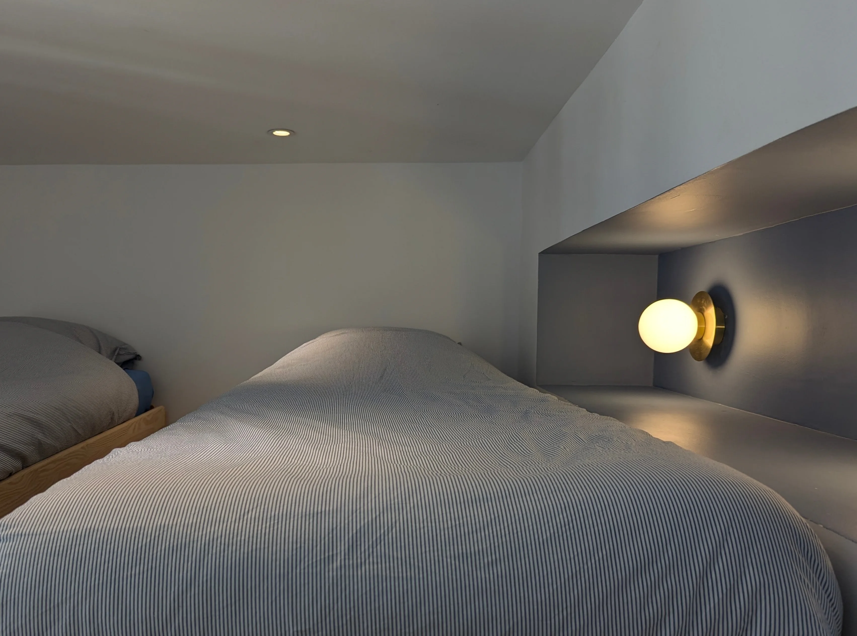 Lit en alcôve sur mesure avec murs bleus, liseuse dorée et linge de lit rayé bleu et blanc.