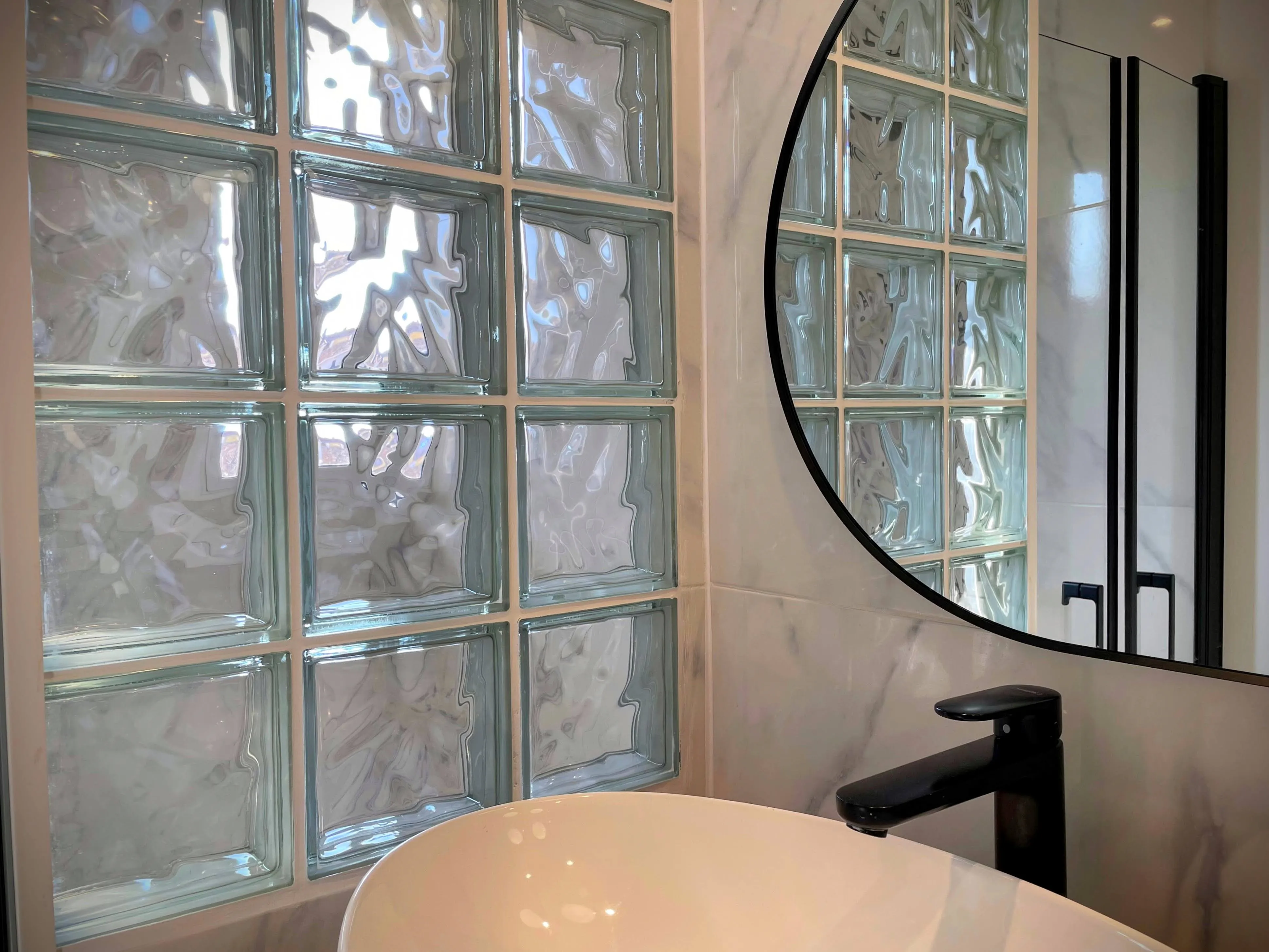 Gros plan miroir rond noir salle de bain reflétant un mur de briques de verre.