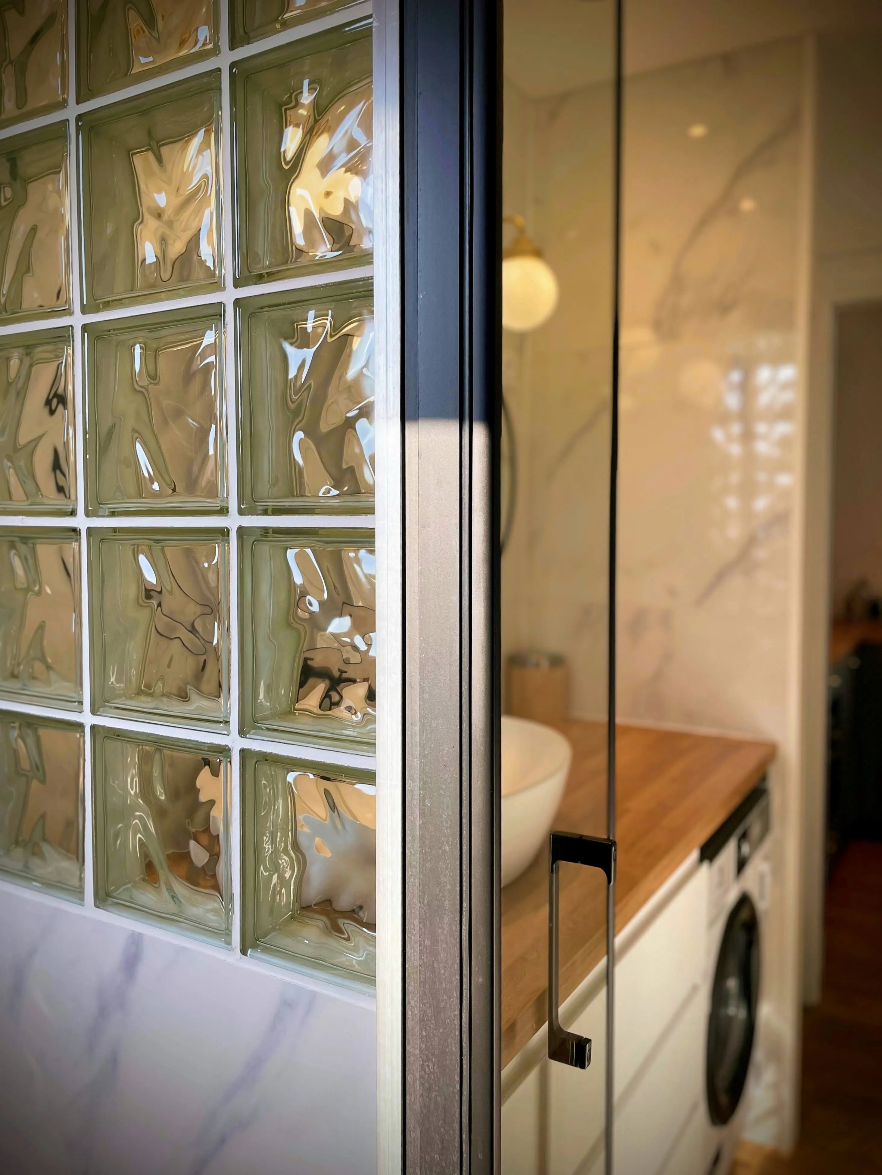 Détail paroi de douche profilé noir et mur en briques de verre ondulées.