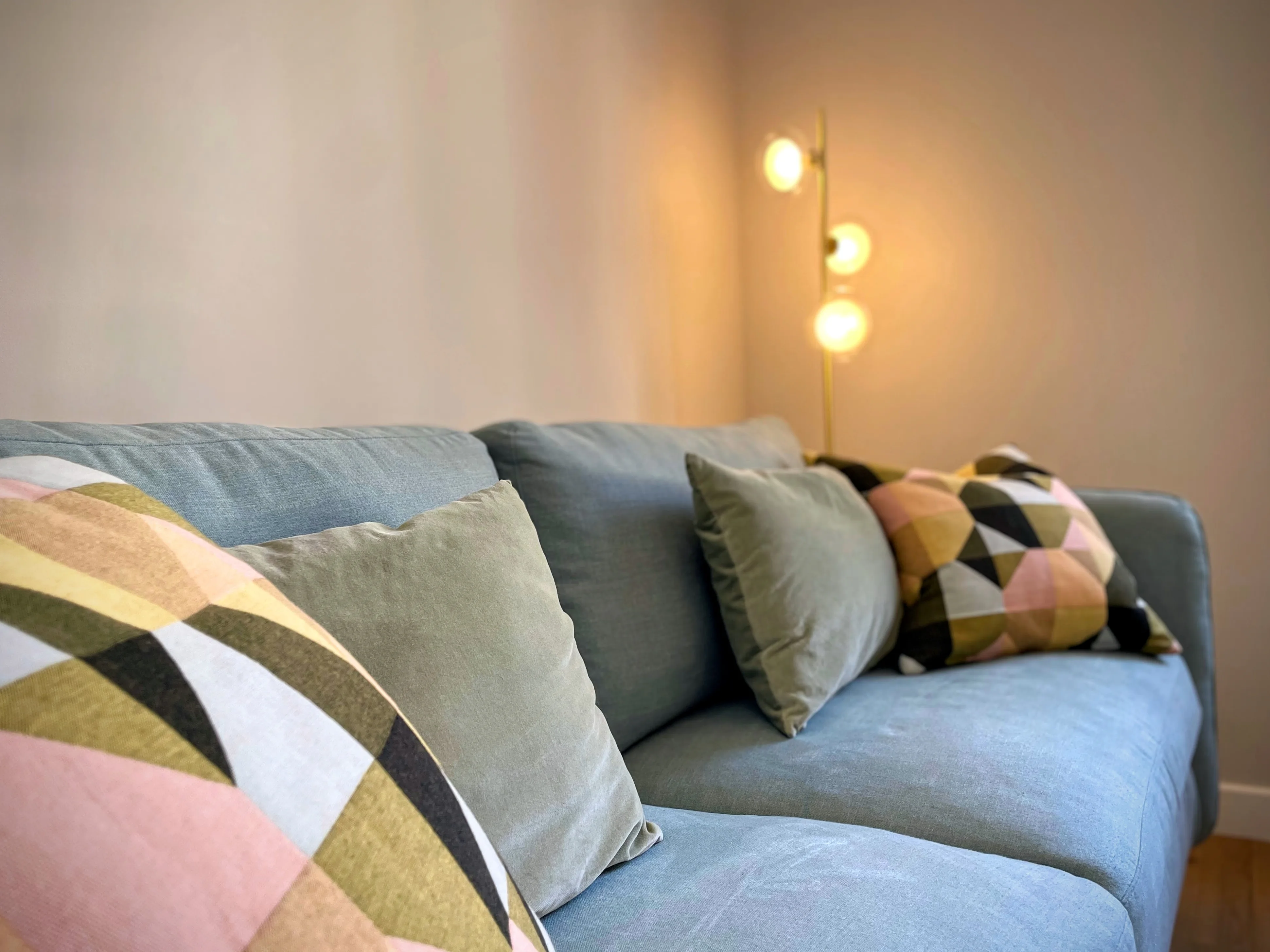 Canapé bleu gris avec coussins motifs géométriques et lampadaire doré en arrière-plan.