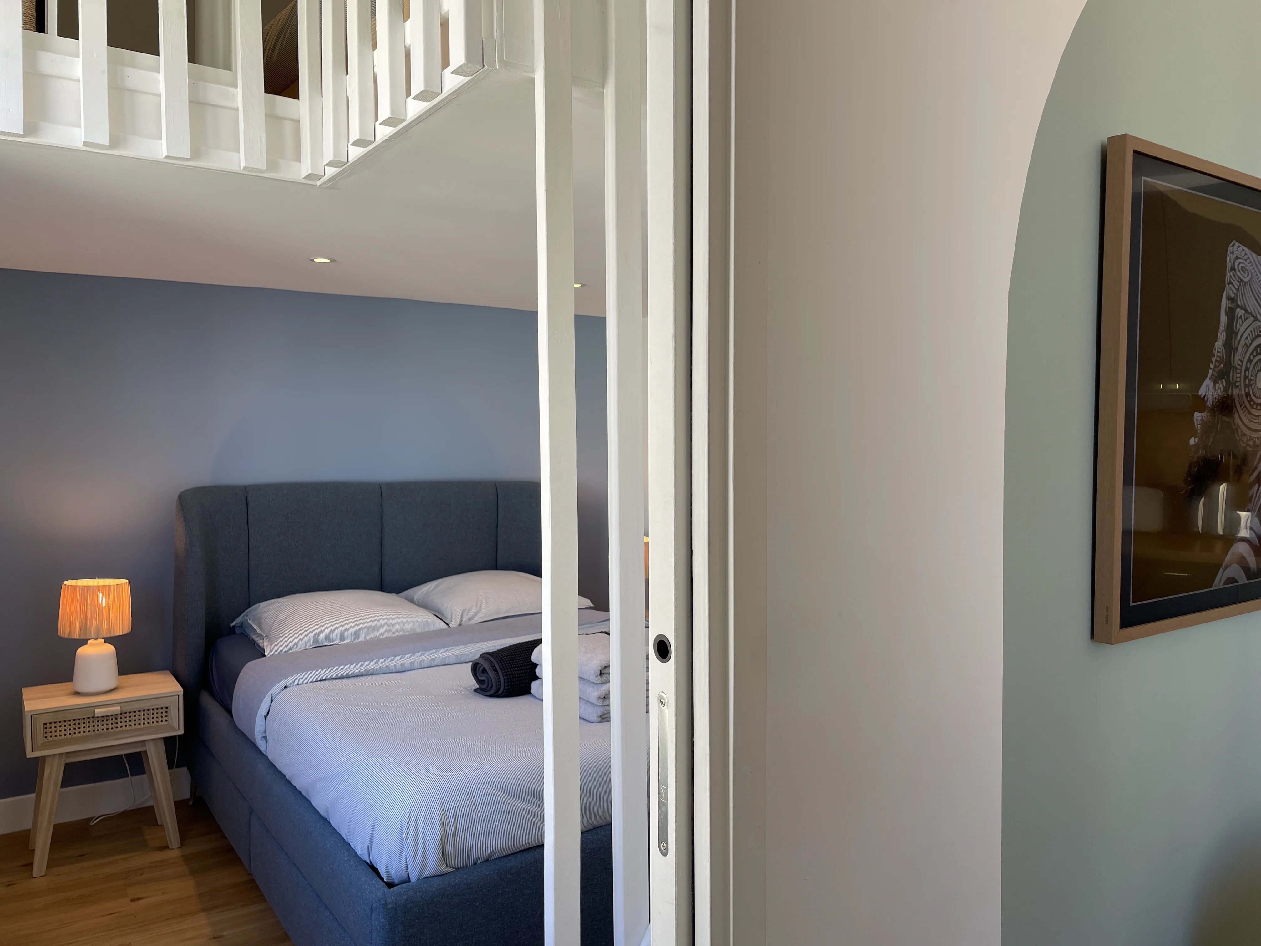Chambre bleue avec lit double et porte coulissante blanche donnant sur pièce de vie.