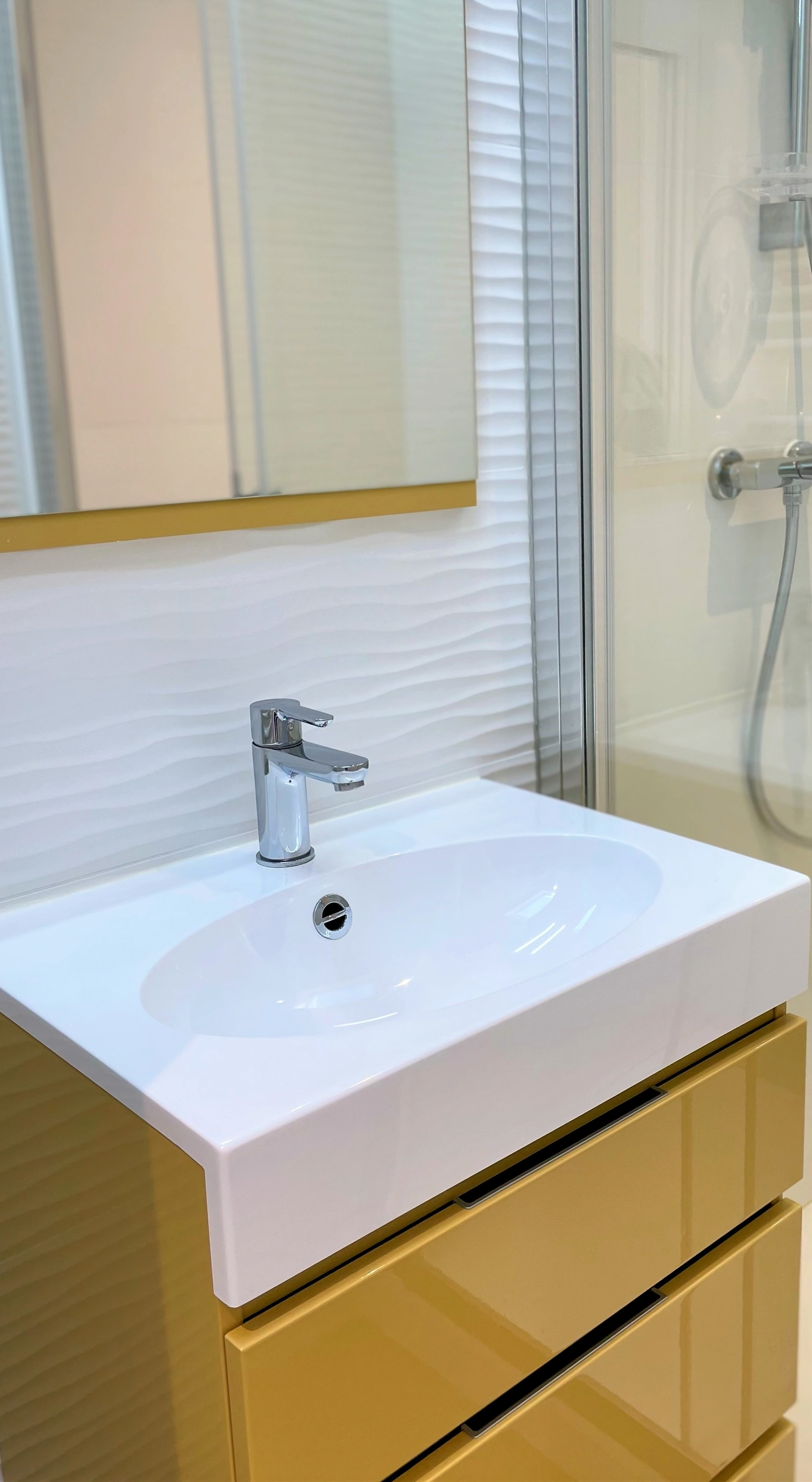 Salle d'eau avec vasque blanche sur meuble jaune moutarde laqué, robinet chromé et douche à l'italienne.