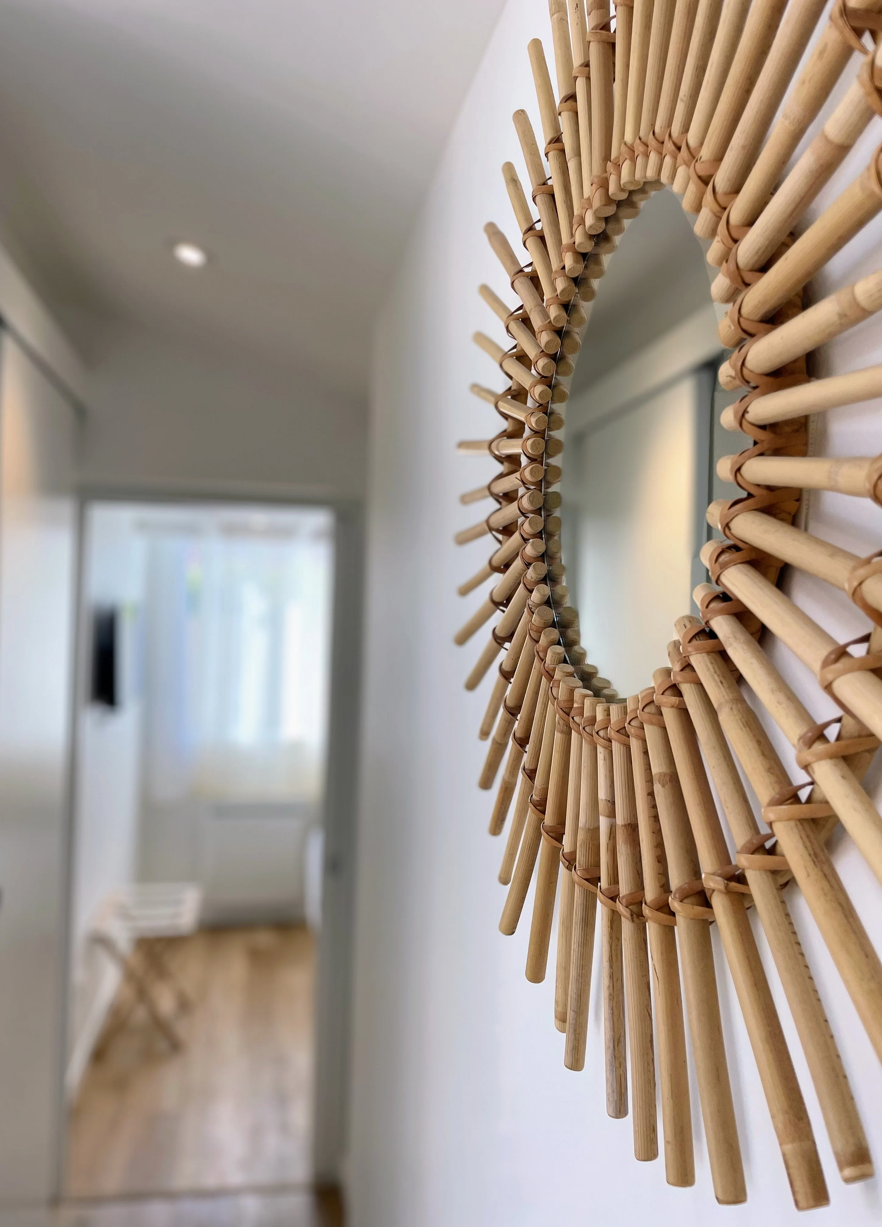 Gros plan sur un miroir soleil en rotin naturel tressé, couloir flouté en arrière-plan.