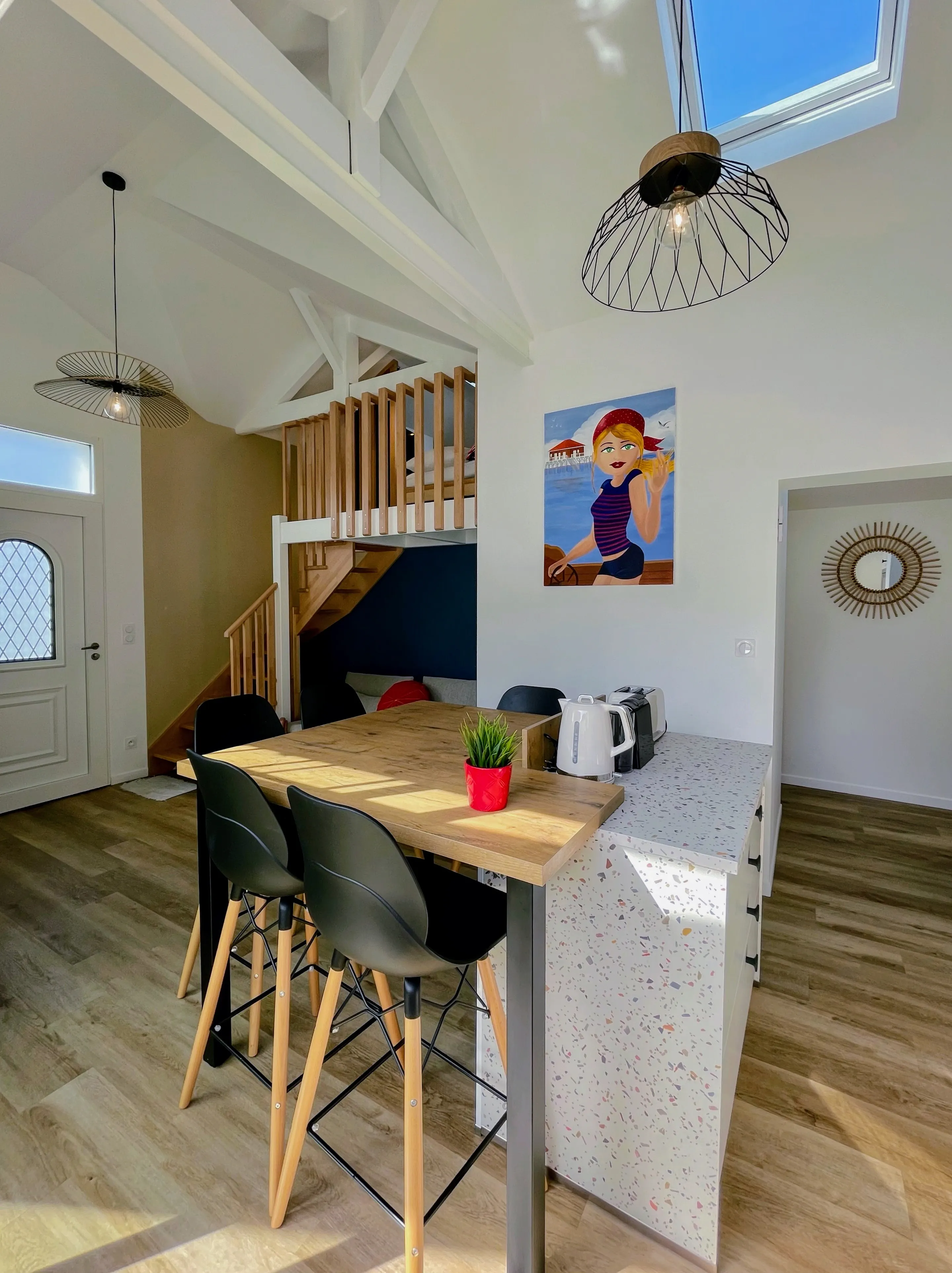 Entrée avec porte vitrée à losanges, suspensions design, mezzanine en bois et tableau d'une baigneuse.