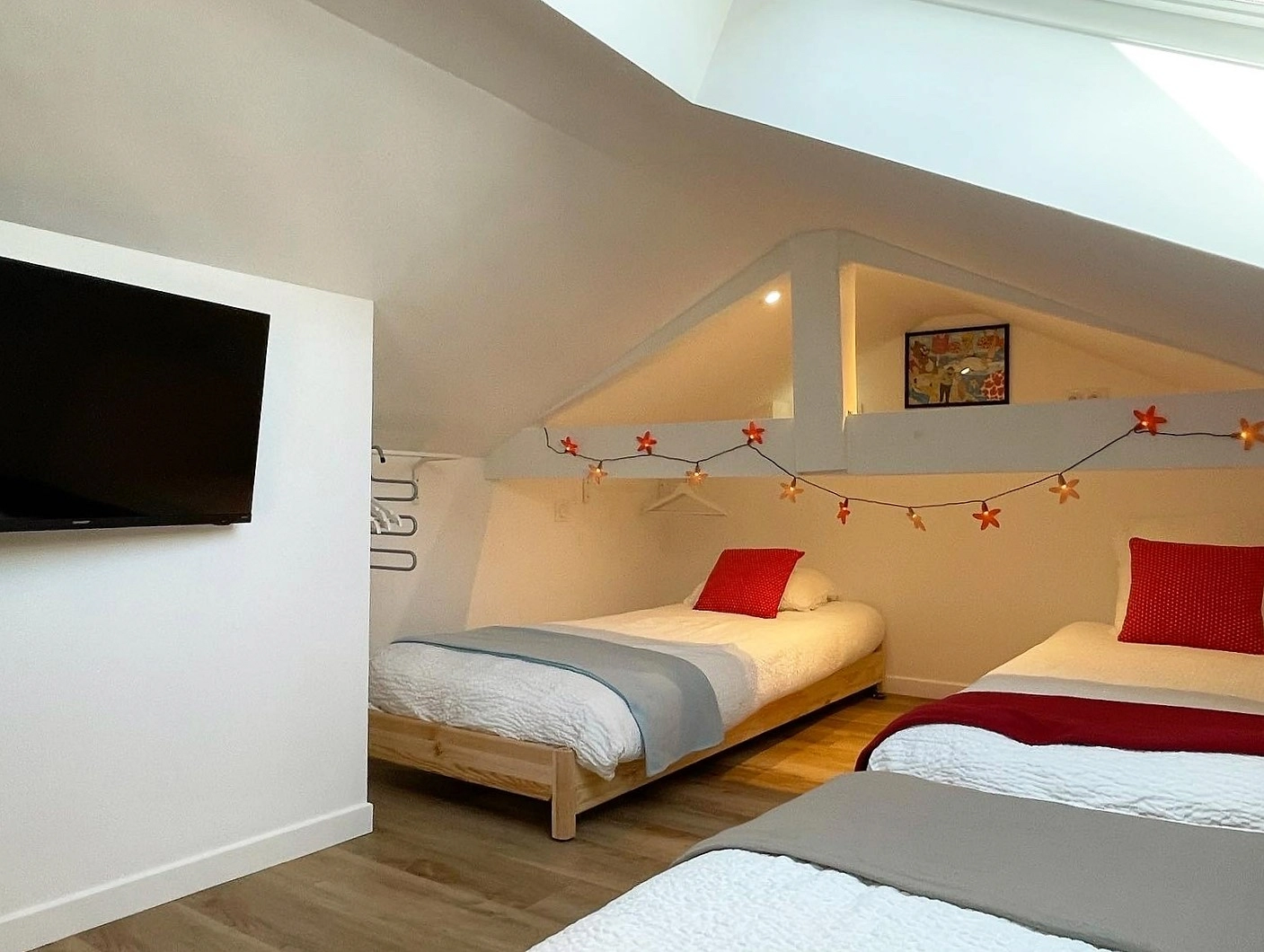 Chambre sous les combles avec deux lits jumeaux, fenêtre de toit et guirlande lumineuse en forme de fleurs.