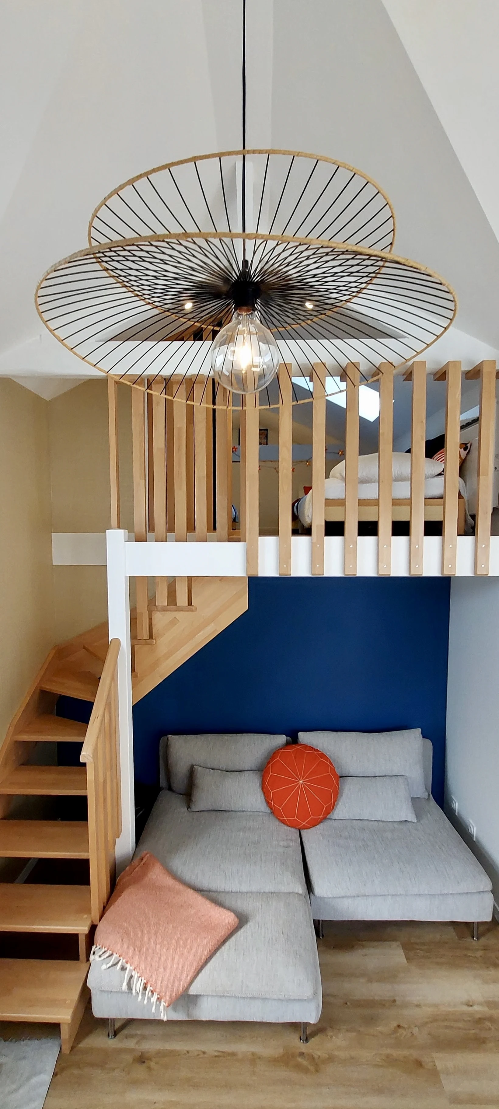 Grande suspension en fibres tressées au-dessus de l'escalier de la mezzanine, canapé à coussin orange.
