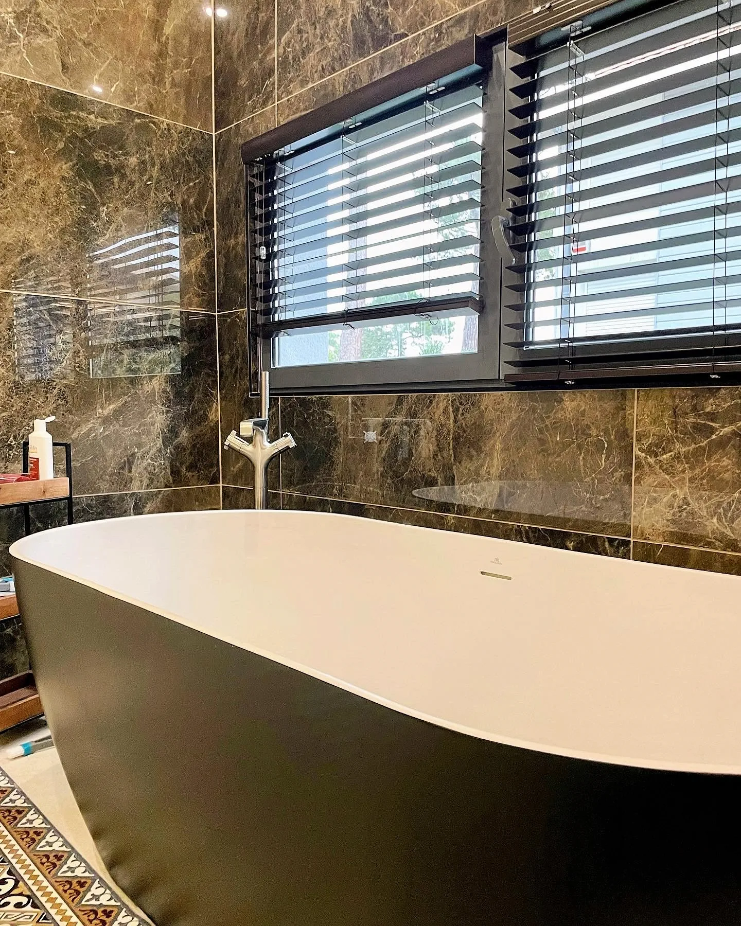 Salle de bain avec baignoire ilot noire et blanche, robinetterie sur pied axor, carrelage mural en marbre