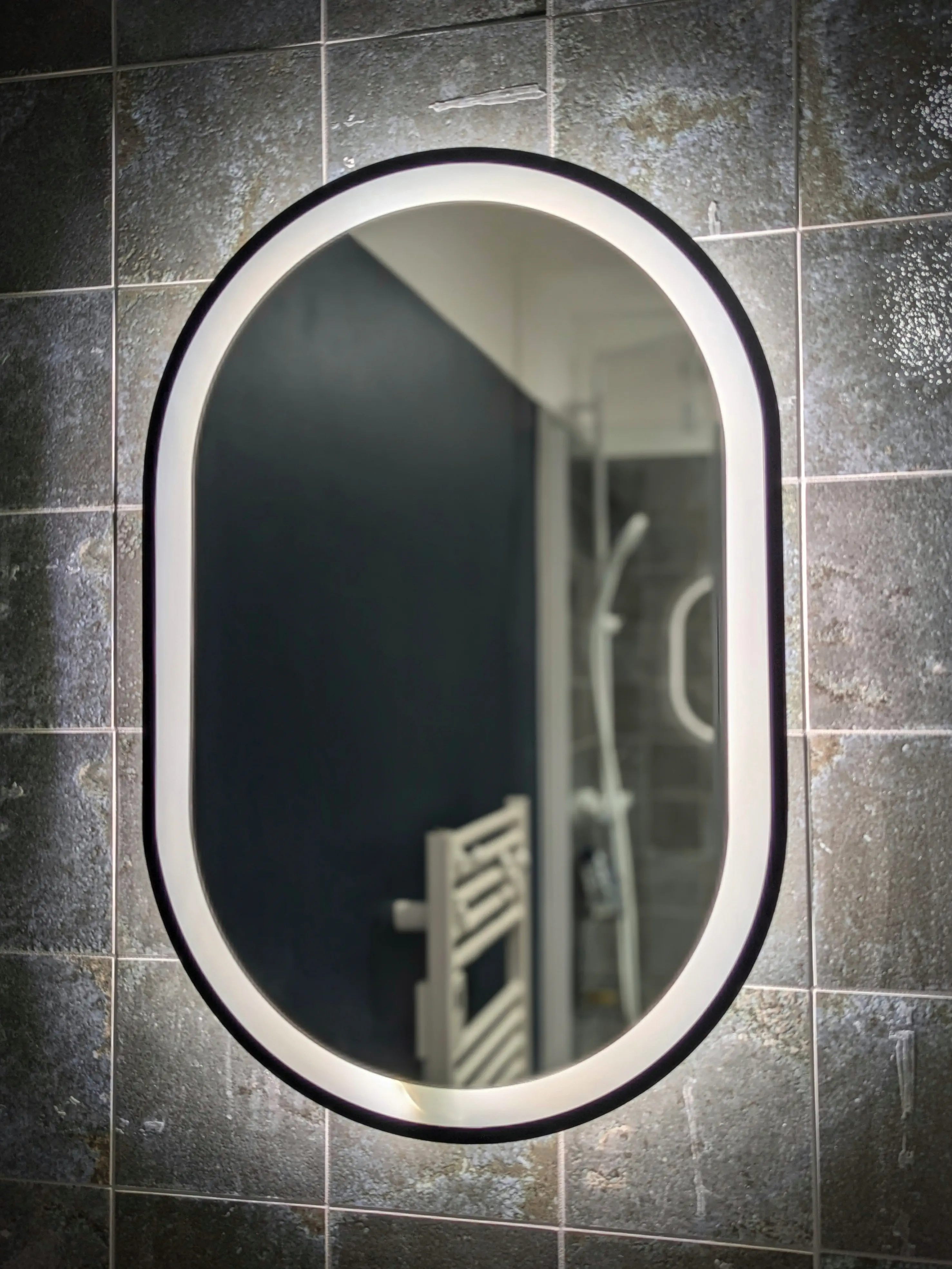 miroir rétroéclairé de forme ovale sur un mur en faïence en terre cuite effet Zellige
