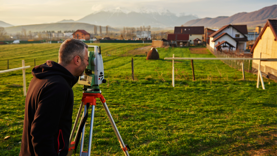 A person is standing in a field with a camera on a tripod