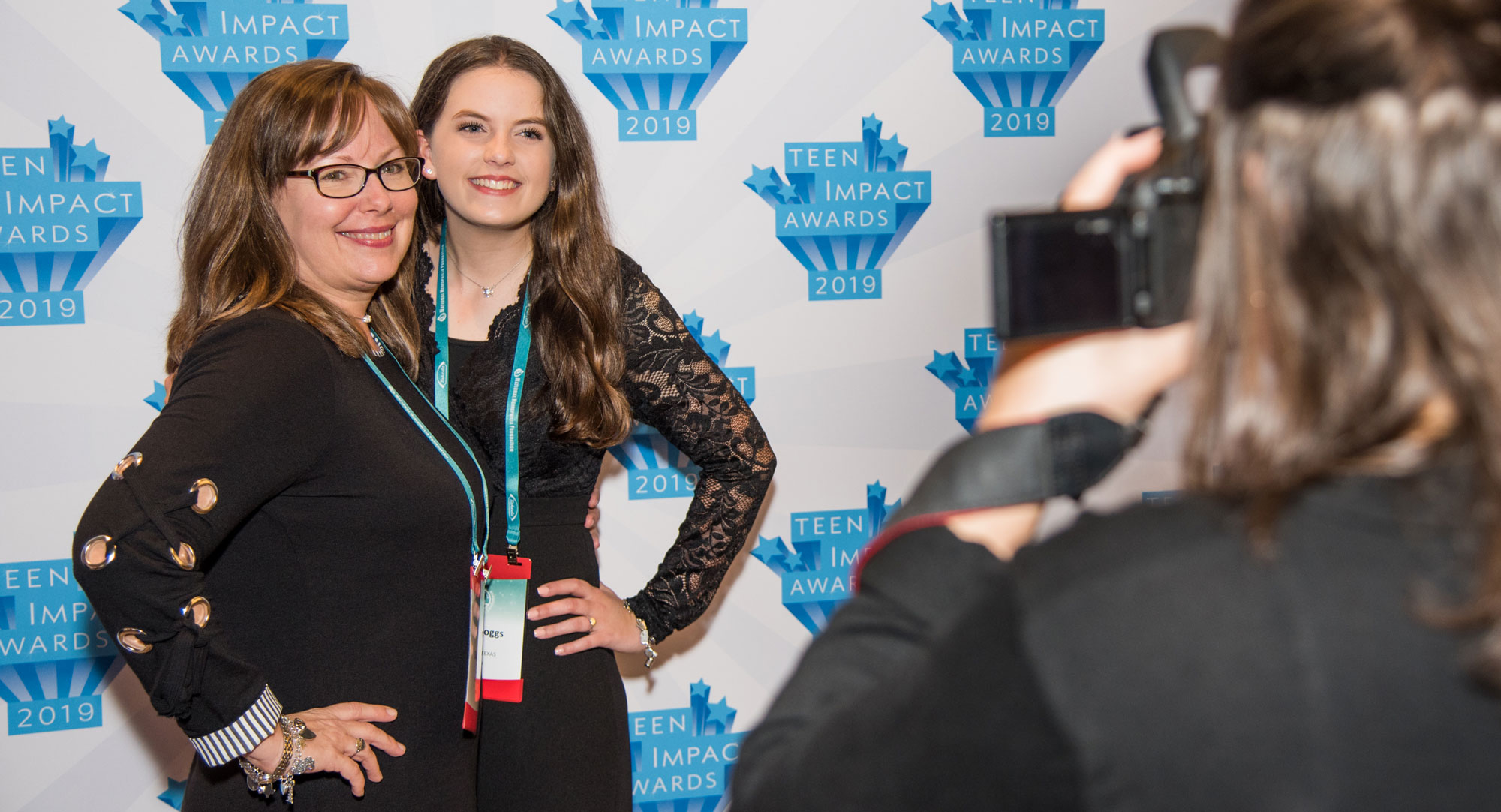 Two guests being photographed against the Teen Impact Awards step-and-repeat banner.