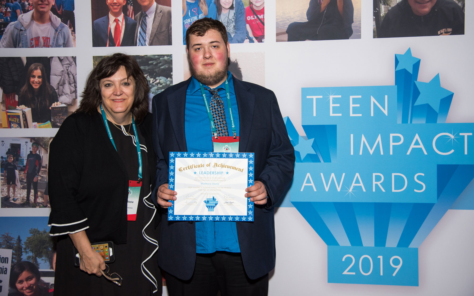 An honoree holding his certificate beside a presenter, in front of the Teen Impact Awards 2019 honoree board.