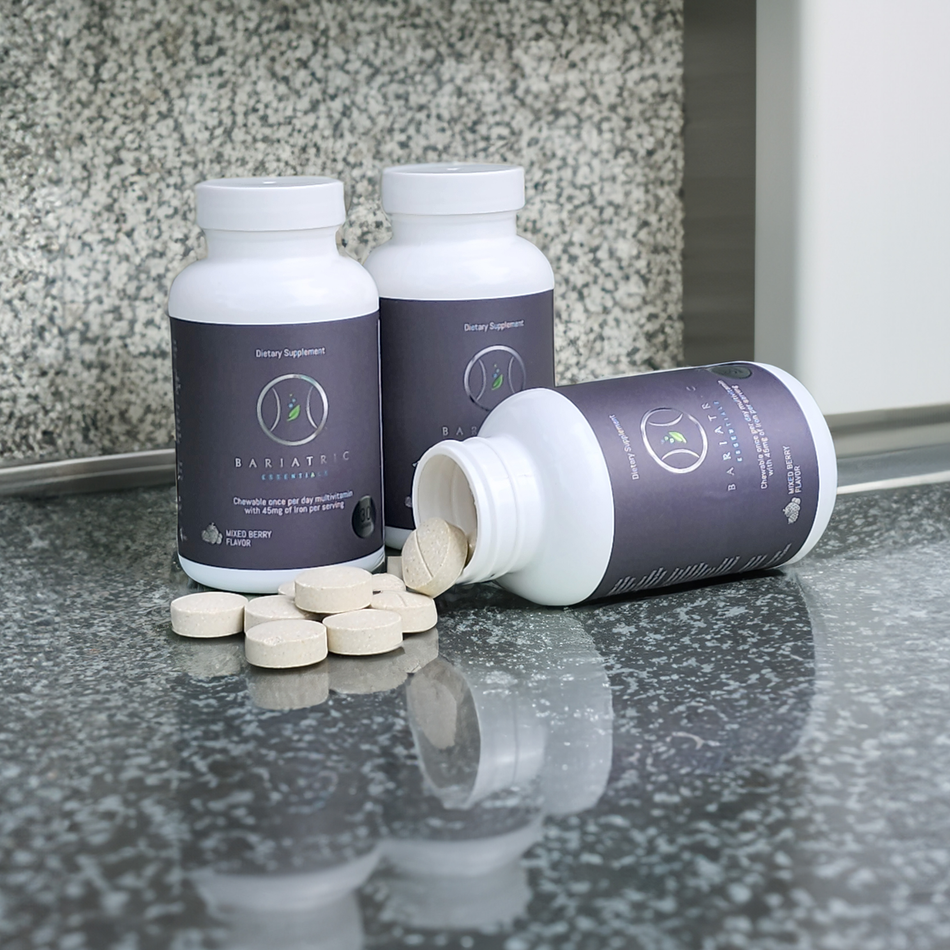 Two Bariatric Essentials bottles upright and a third on its side, chewable tablets spilling onto a granite counter.