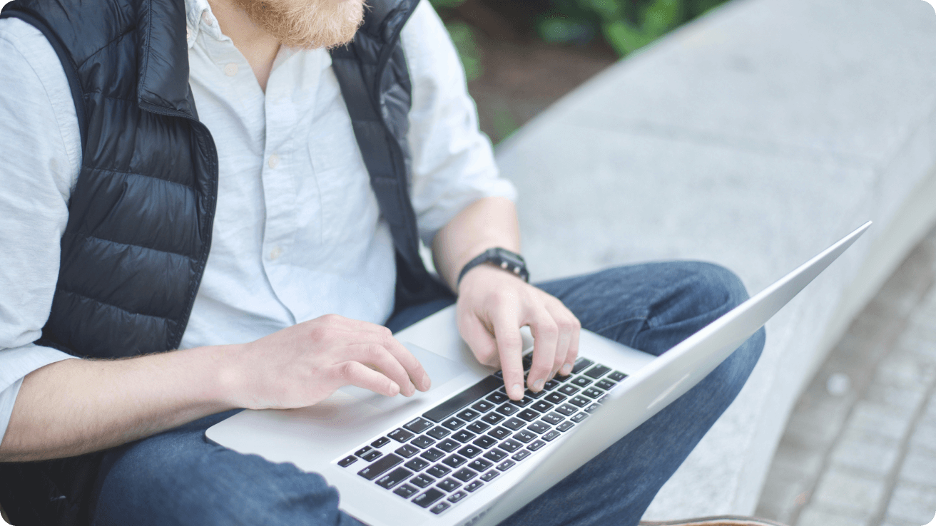 A man sitting outside on a concrete step using a laptop keyboard.