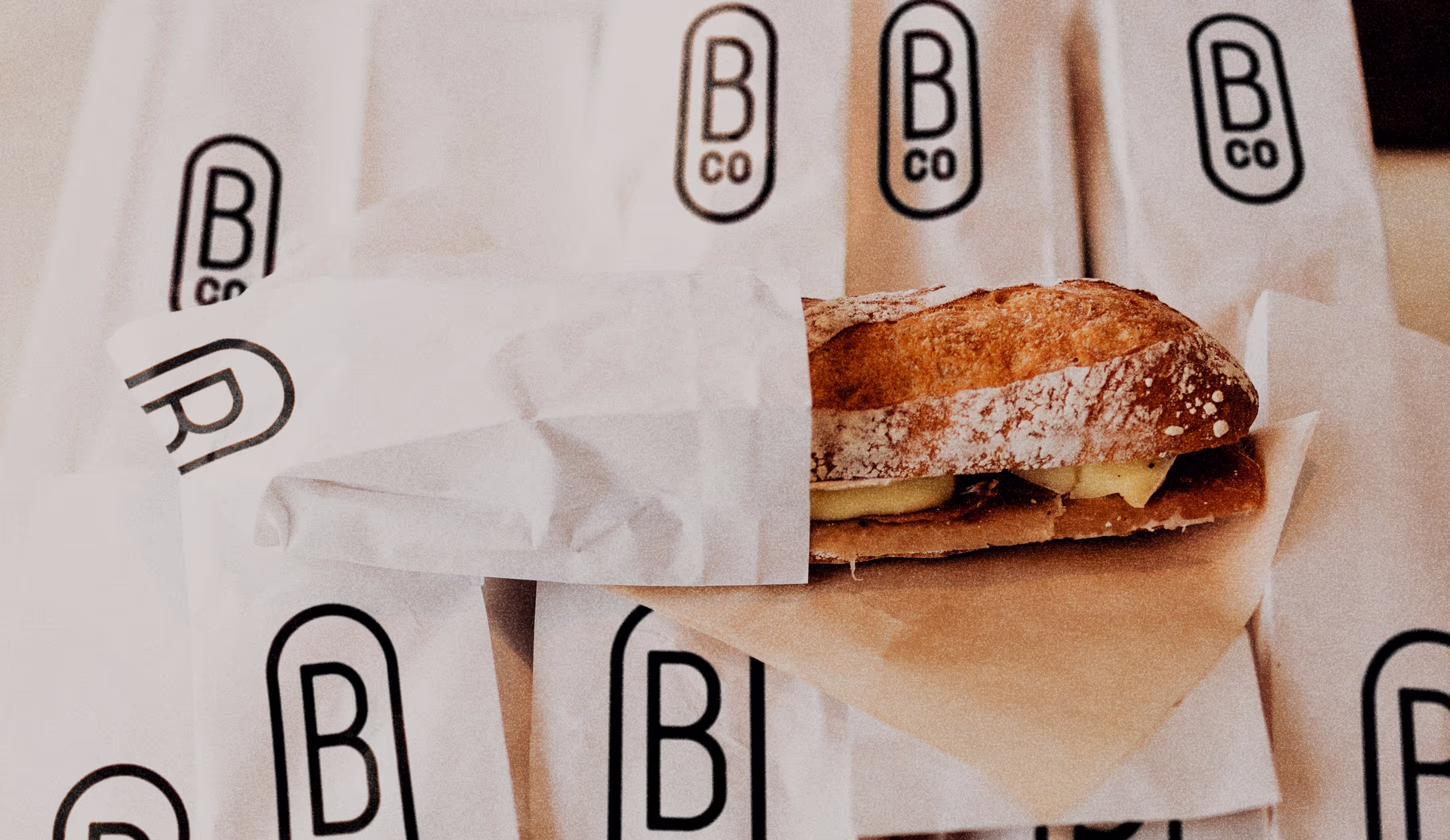 Allemaal papieren broodzakjes met daarop het symbool van Broodjes & Co. In één zak zit een broodje.