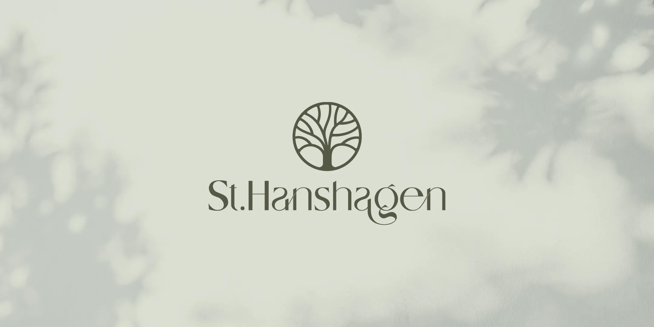 St. Hanshagen-logo med stilisert tre i sirkel på lys bakgrunn med skygger.