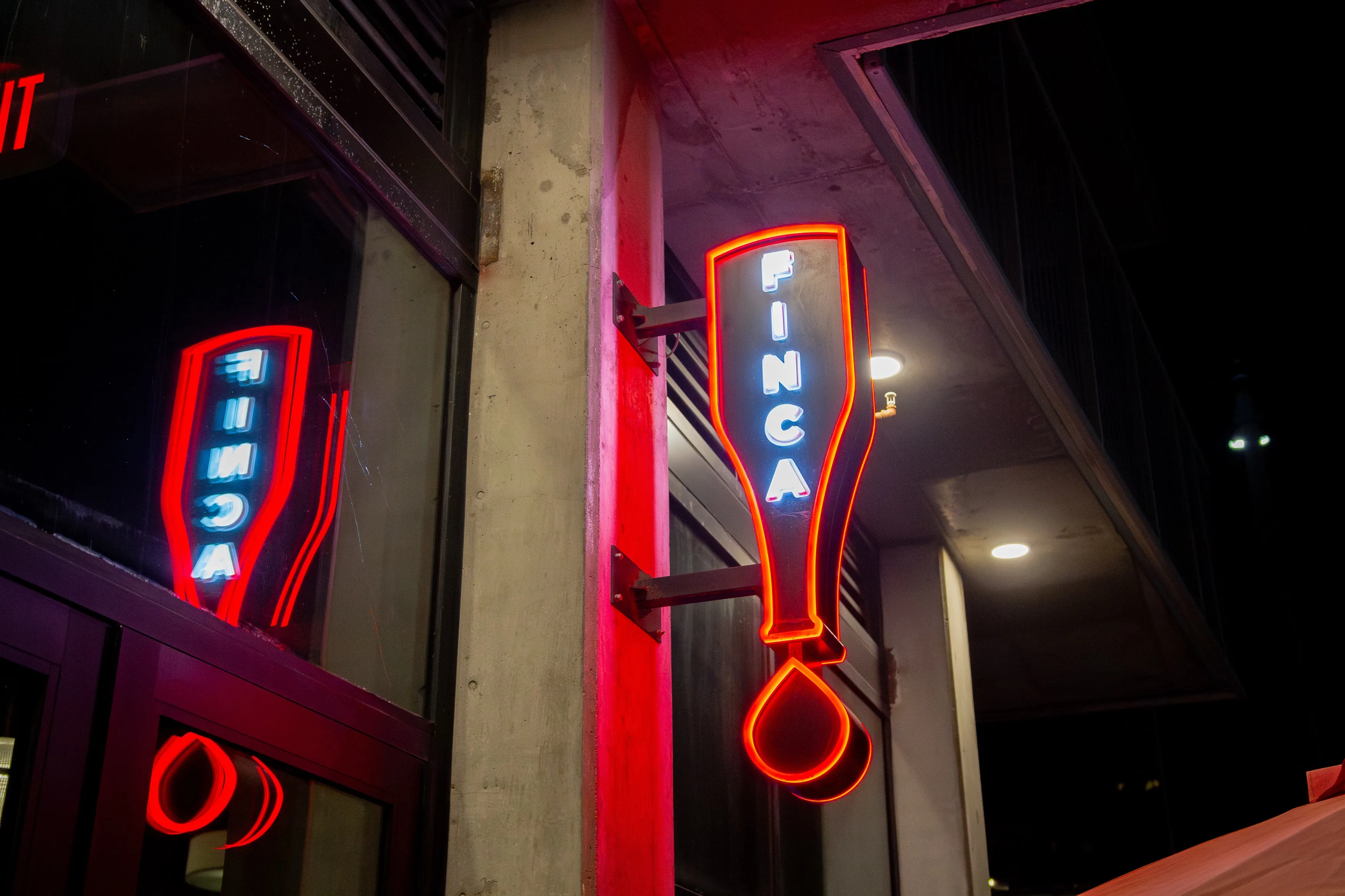 Neon sign shaped like an upside-down bottle with the word 'FINCA' glowing in blue outlined by red neon light on a building wall at night.