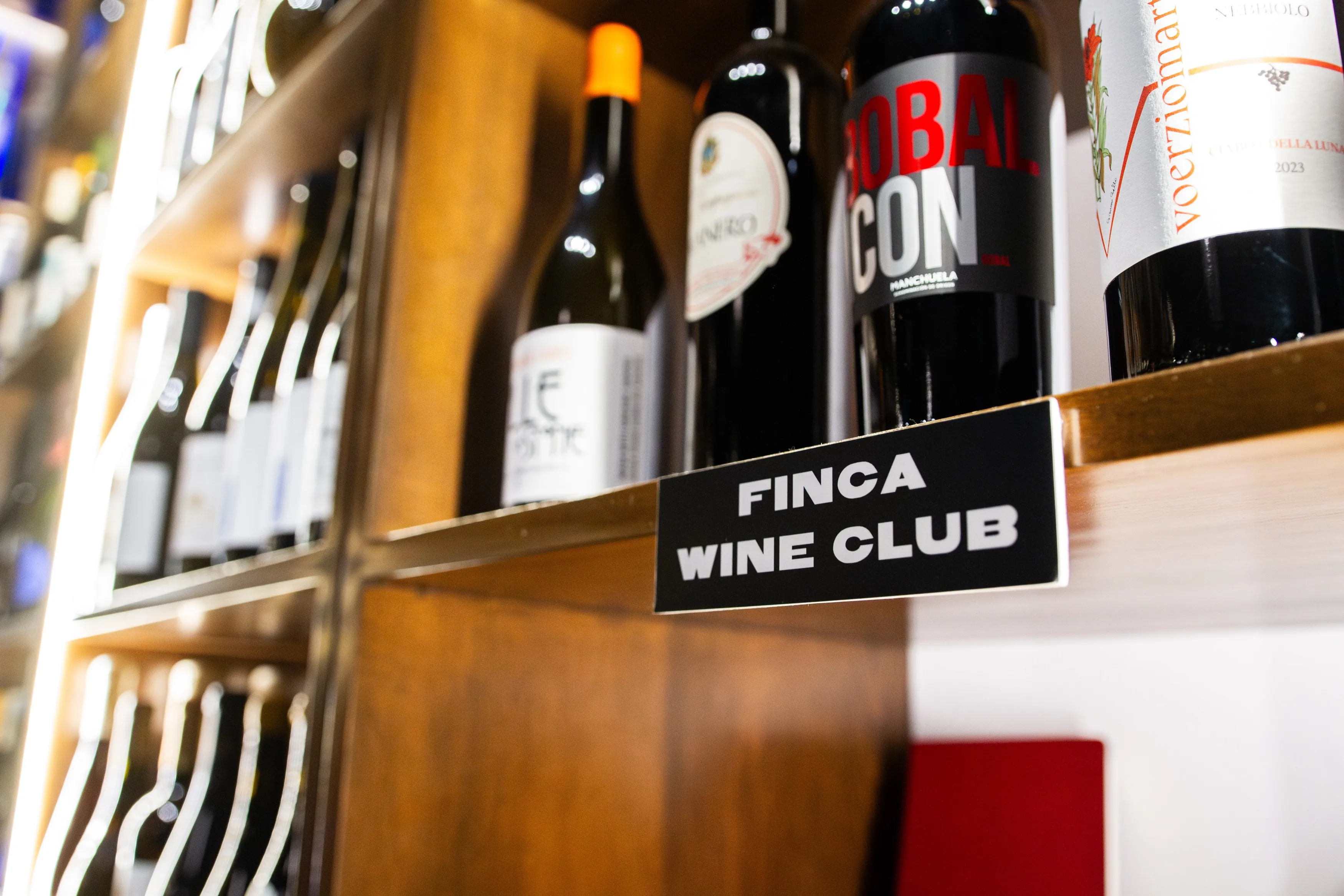 Shelf with multiple wine bottles and a sign reading 'FINCA WINE CLUB' in a wooden wine rack.