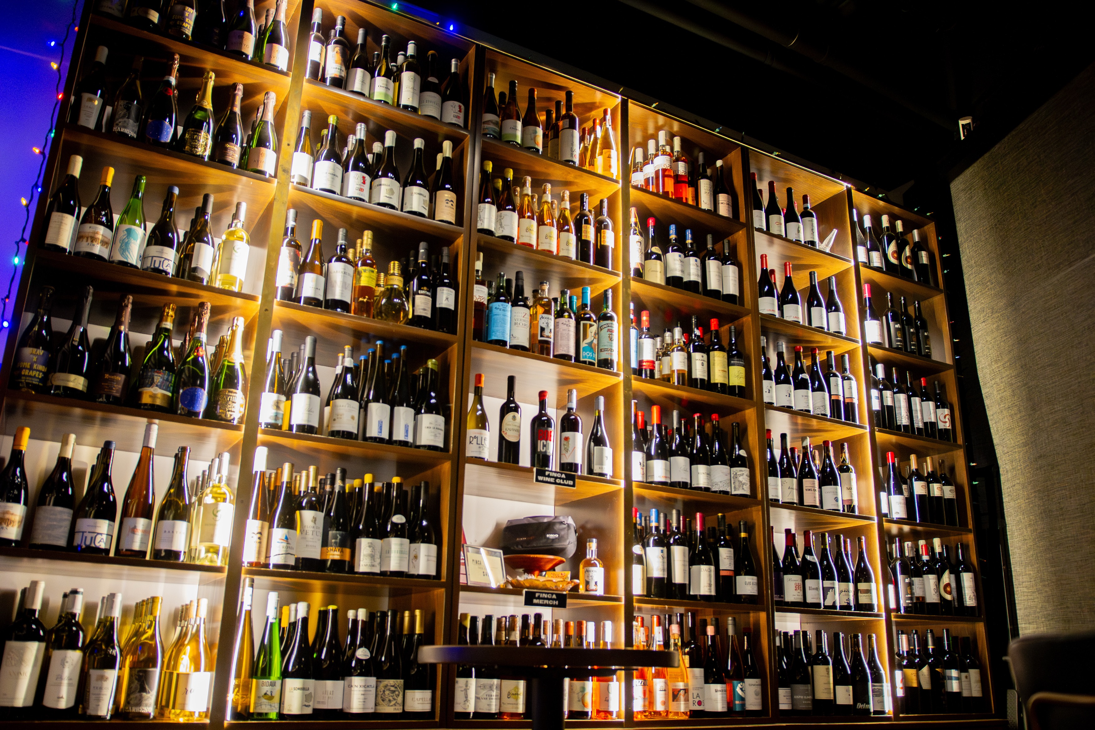 Backlit wooden shelves filled with numerous bottles of wine in a wine shop or bar.