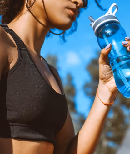 Woman in black sports bra holding a blue water bottle outdoors under a clear blue sky.