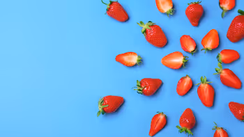 Whole and halved strawberries scattered on a blue background.