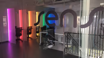 Modern office interior with colorful vertical LED light strips and the word 'sens' displayed on glass walls.