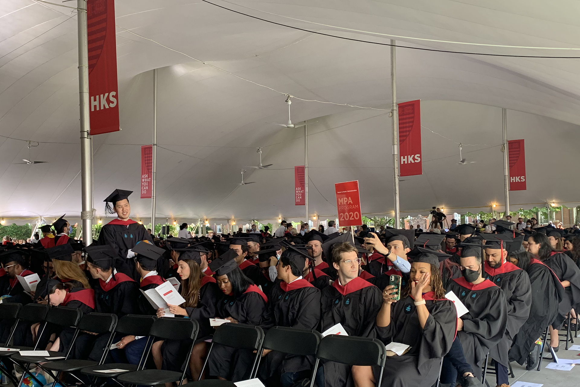 HKS graduating students sitting under Commencement tent with pole banners above them
