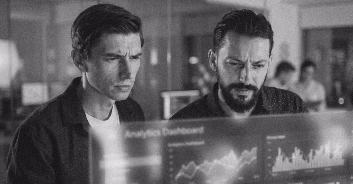 Two individuals intently examine a futuristic holographic display showing an analytics dashboard with charts and graphs.
