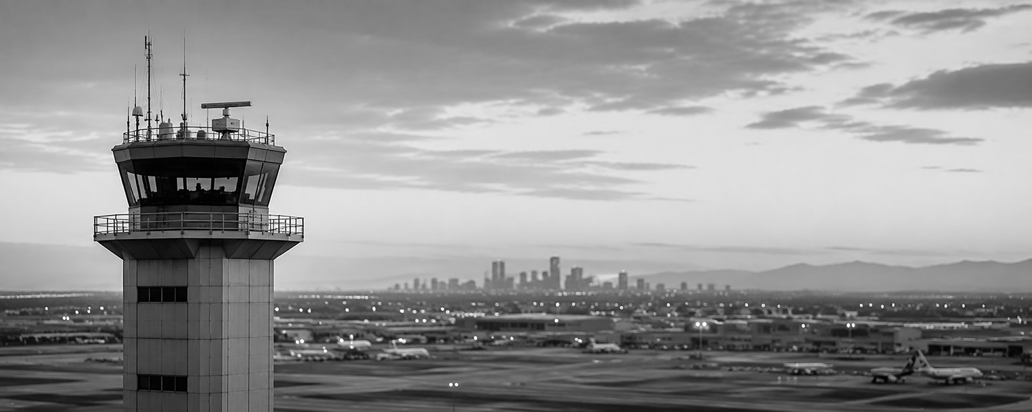 Airport air traffic control tower overlooking runways and a distant city skyline.