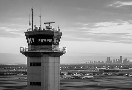 Air traffic control tower overlooking an airport and distant city skyline.