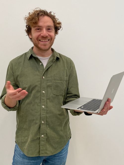 Photo of Max laughing and holding a laptop