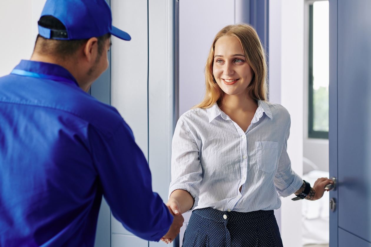 Smiling woman opens her front door to greet a uniformed service technician.