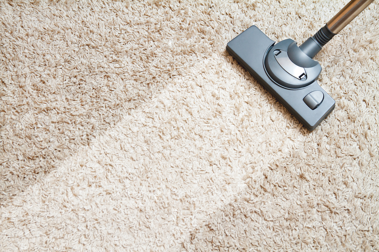 Technician using a vacuum cleaner to deep clean a long beige carpet in a modern home.