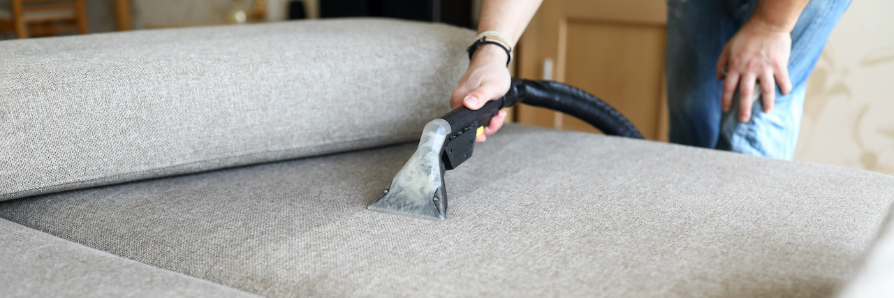 Professional using steam vapor equipment to clean a beige sofa in a modern living room.