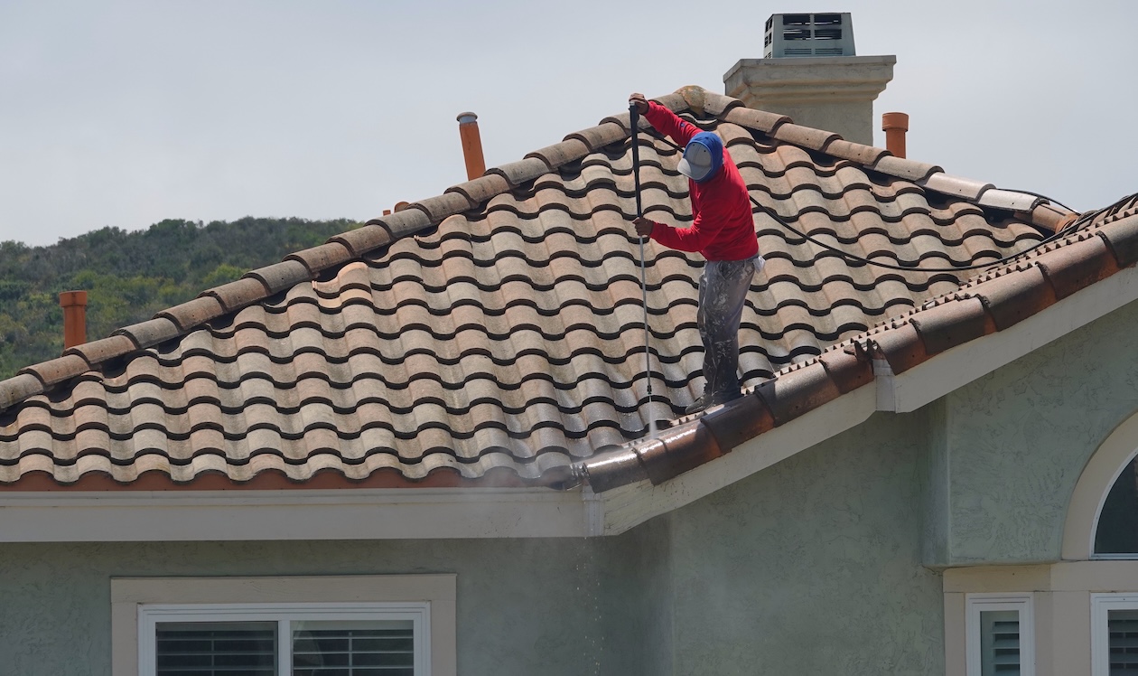 Worker using a pressure washer to clean a home’s tile roof, removing dirt and debris during an exterior cleaning job.